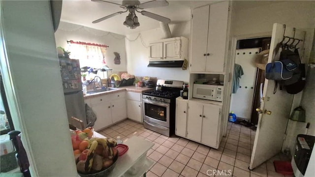 kitchen featuring stainless steel gas stove, light tile patterned flooring, white microwave, under cabinet range hood, and a sink