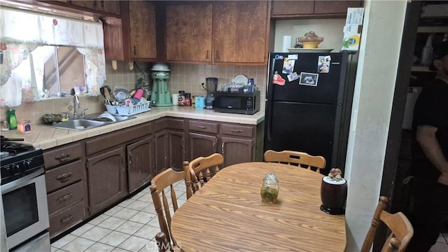 kitchen featuring a sink, tile countertops, backsplash, and black appliances