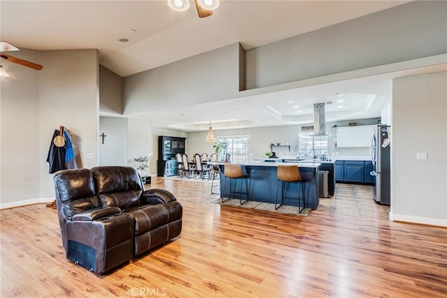 living room with a tray ceiling, baseboards, a ceiling fan, and light wood-style floors