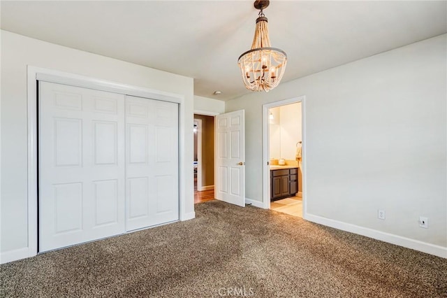 unfurnished bedroom with a closet, baseboards, ensuite bathroom, a chandelier, and light colored carpet