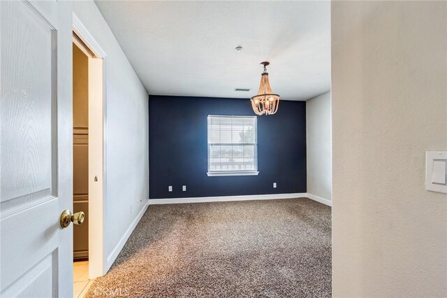 carpeted spare room featuring a chandelier, visible vents, and baseboards