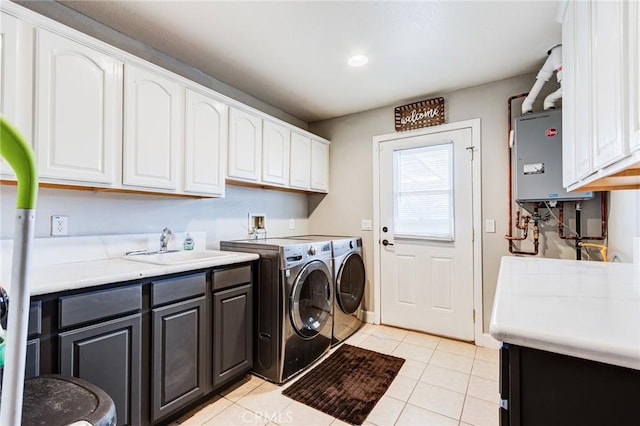 laundry area with tankless water heater, light tile patterned flooring, washer and clothes dryer, cabinet space, and a sink