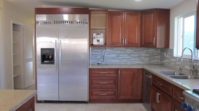kitchen featuring appliances with stainless steel finishes, tasteful backsplash, brown cabinets, a sink, and light tile patterned flooring