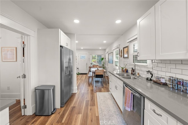kitchen with white cabinets, stainless steel appliances, light wood-style flooring, and a sink