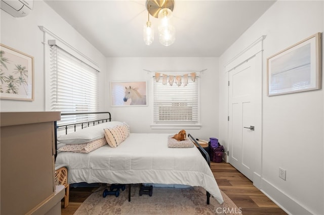bedroom with wood finished floors, an AC wall unit, and baseboards