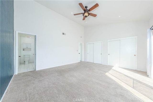 unfurnished bedroom with ensuite bath, two closets, carpet floors, visible vents, and high vaulted ceiling