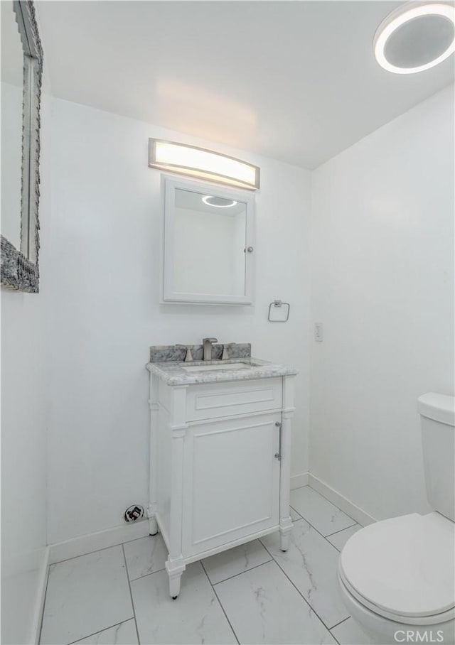 half bathroom featuring toilet, marble finish floor, vanity, and baseboards