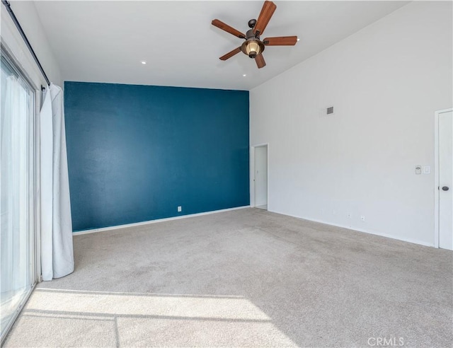 carpeted empty room with a high ceiling, a ceiling fan, and visible vents