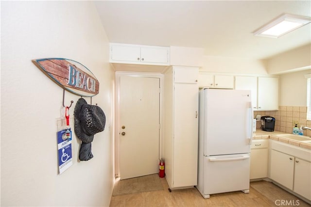 4433 Albatross Way, Oceanside, CA 92057 - kitchen featuring freestanding refrigerator, tile counters, a sink, decorative backsplash, and white cabinets