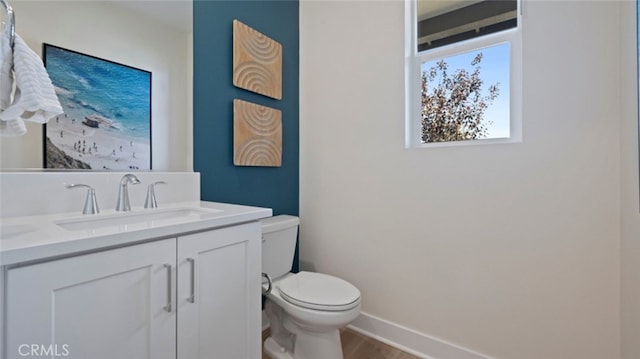 half bathroom with toilet, vanity, baseboards, and wood finished floors