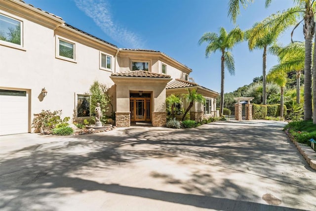 mediterranean / spanish house with stucco siding, stone siding, driveway, and a tiled roof