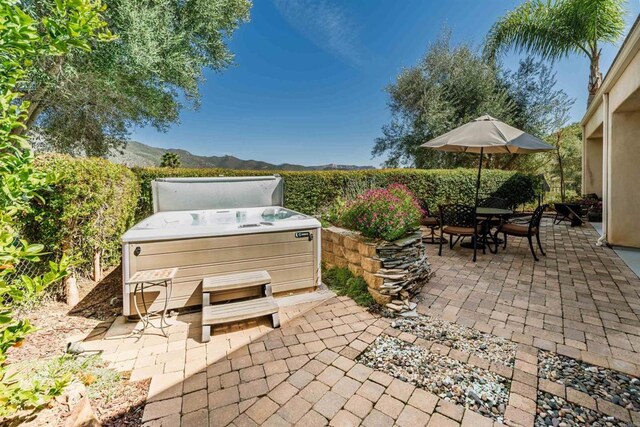 view of patio with outdoor dining area, a mountain view, and a hot tub