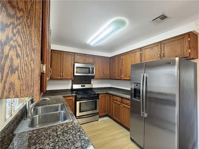 2414 Grove Ave, San Diego, CA 92154 - kitchen with stainless steel appliances, a sink, dark countertops, a textured ceiling, and light wood finished floors