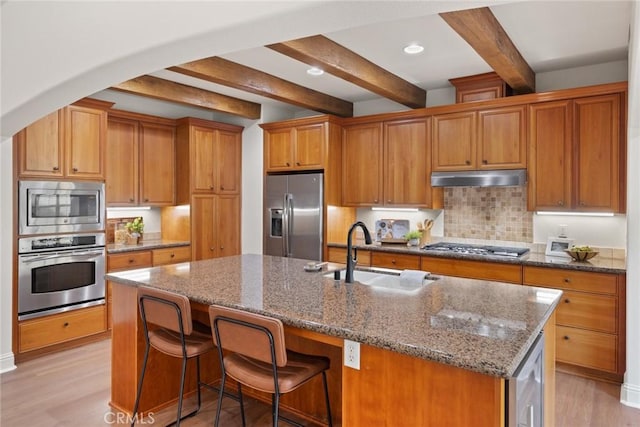 kitchen featuring an island with sink, under cabinet range hood, a sink, wine cooler, and appliances with stainless steel finishes