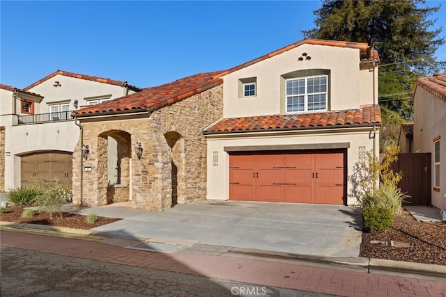 mediterranean / spanish-style house featuring stucco siding, a tile roof, concrete driveway, a garage, and a balcony
