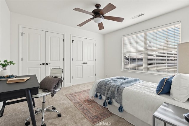 carpeted bedroom with visible vents, two closets, and a ceiling fan