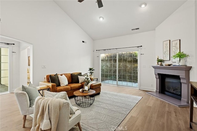 living room featuring visible vents, wood finished floors, a glass covered fireplace, high vaulted ceiling, and a ceiling fan