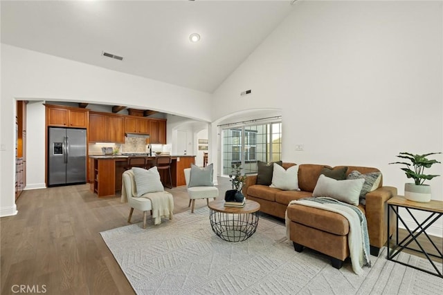 living area featuring visible vents, baseboards, light wood-style floors, arched walkways, and high vaulted ceiling