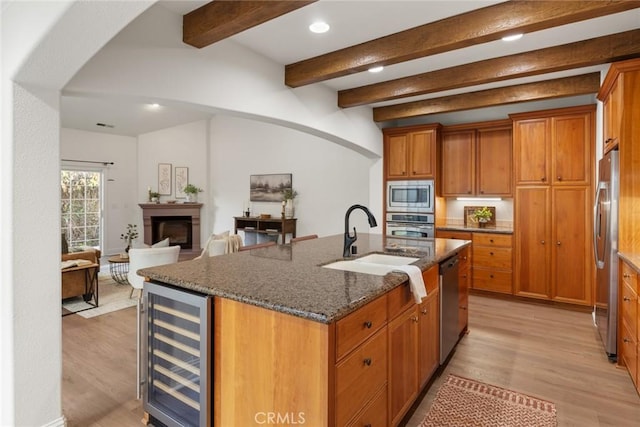 kitchen with an island with sink, beverage cooler, a sink, stainless steel appliances, and arched walkways