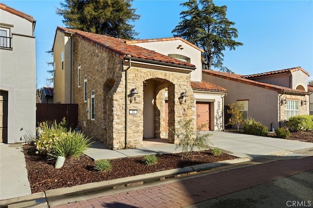 mediterranean / spanish house featuring stucco siding, concrete driveway, a garage, stone siding, and a tiled roof