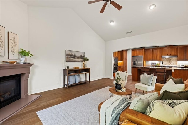 living area with visible vents, baseboards, ceiling fan, wood finished floors, and high vaulted ceiling