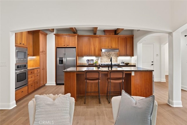 kitchen with tasteful backsplash, under cabinet range hood, arched walkways, stainless steel appliances, and a sink