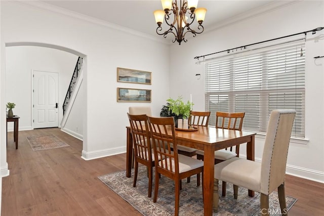 dining area featuring wood finished floors, arched walkways, an inviting chandelier, crown molding, and baseboards