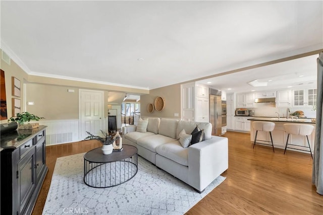 living area featuring light wood-style flooring, a wainscoted wall, ornamental molding, and recessed lighting