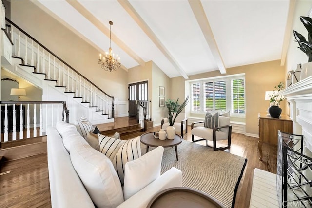 living area with stairs, a notable chandelier, vaulted ceiling with beams, a fireplace, and wood finished floors