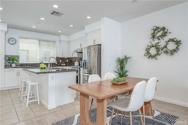 kitchen with stainless steel appliances, a center island with sink, decorative backsplash, a sink, and white cabinets