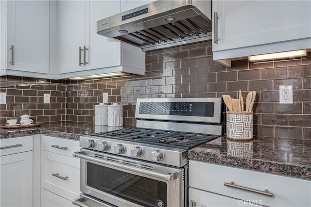 kitchen with range hood, stainless steel range with gas cooktop, tasteful backsplash, white cabinetry, and dark stone countertops