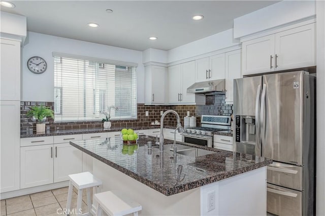 kitchen with appliances with stainless steel finishes, under cabinet range hood, white cabinetry, a sink, and backsplash