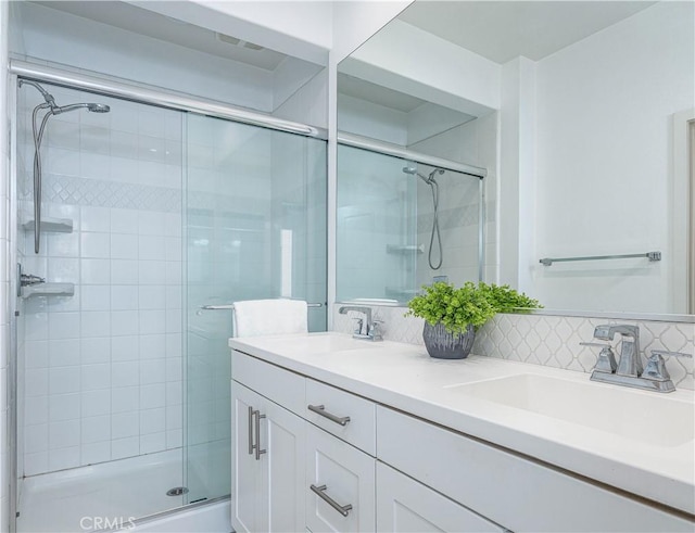 bathroom featuring a stall shower, double vanity, and tasteful backsplash