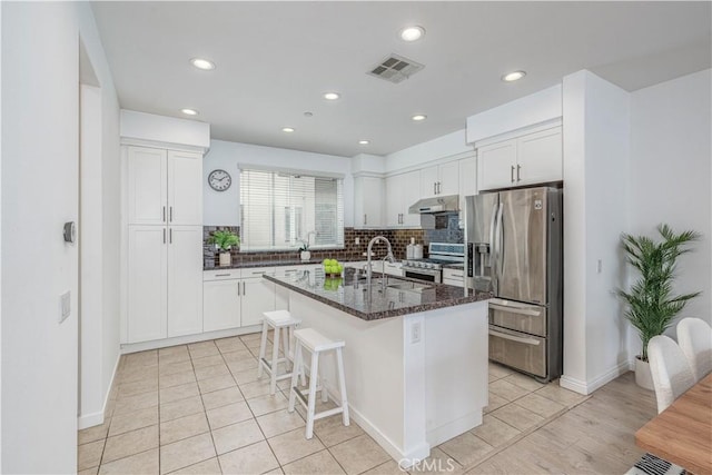 kitchen featuring stainless steel appliances, a sink, under cabinet range hood, white cabinetry, and backsplash