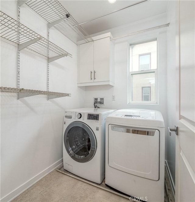 clothes washing area featuring washing machine and dryer, cabinet space, and baseboards