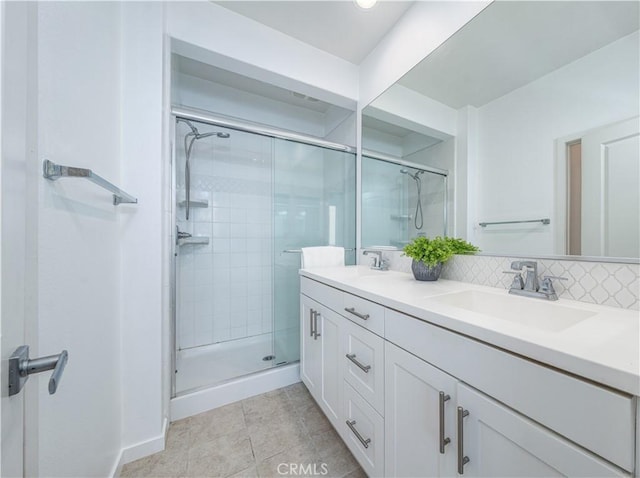 bathroom featuring a shower stall, double vanity, tile patterned flooring, and baseboards