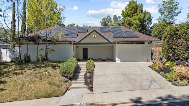 ranch-style home featuring roof mounted solar panels, fence, stucco siding, a front lawn, and driveway