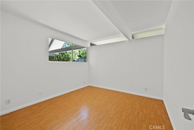 unfurnished room featuring wood finished floors, baseboards, and beam ceiling