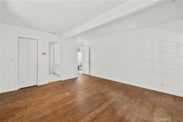 unfurnished bedroom with baseboards, ensuite bath, visible vents, beamed ceiling, and wood-type flooring