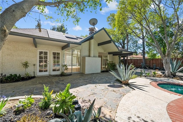 rear view of house with a patio, stucco siding, a jacuzzi, fence, and roof mounted solar panels