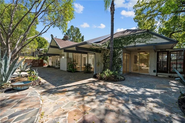 back of property featuring roof mounted solar panels, a patio area, stucco siding, and a chimney