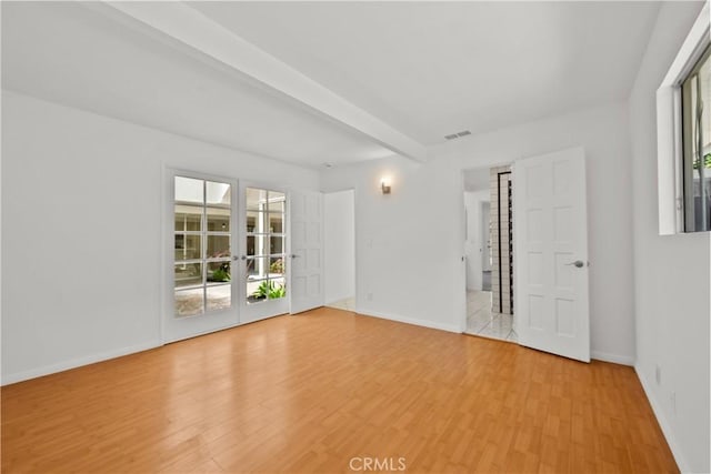 spare room featuring visible vents, baseboards, light wood-type flooring, beamed ceiling, and french doors