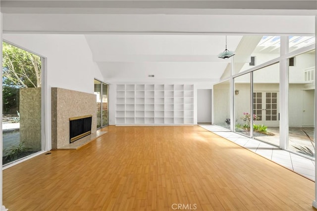 unfurnished living room with built in features, a fireplace with raised hearth, wood finished floors, and lofted ceiling with beams