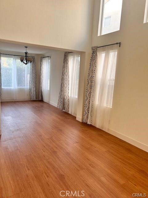 spare room featuring light wood finished floors, a notable chandelier, a high ceiling, and baseboards