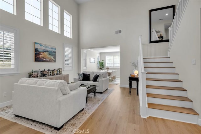 living room with visible vents, baseboards, stairway, and light wood-type flooring