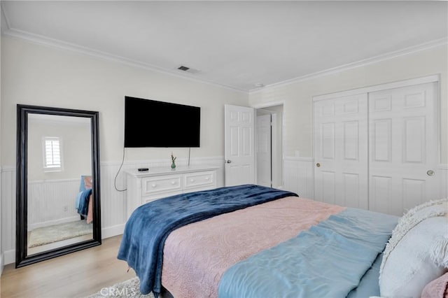 bedroom with a closet, a wainscoted wall, ornamental molding, and light wood-style floors
