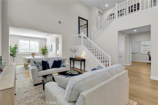 living area with plenty of natural light, visible vents, a high ceiling, and wood finished floors