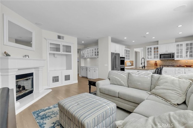 living room with visible vents, a glass covered fireplace, light wood finished floors, and recessed lighting