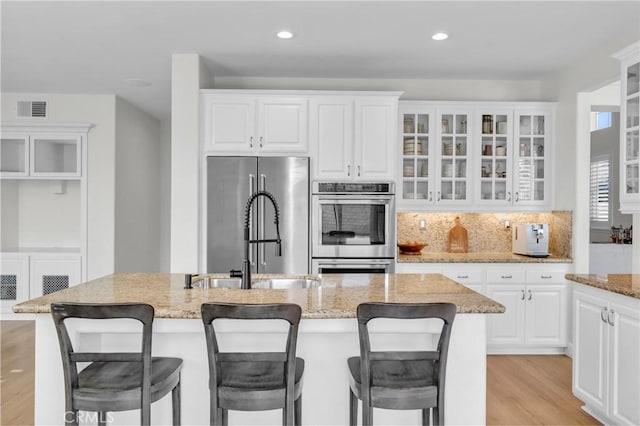 kitchen with a sink, backsplash, appliances with stainless steel finishes, visible vents, and light wood-style floors