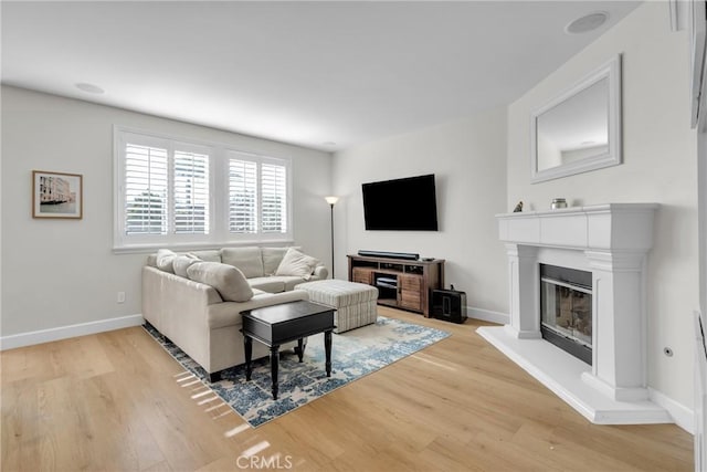 living room featuring a glass covered fireplace, light wood-style floors, and baseboards